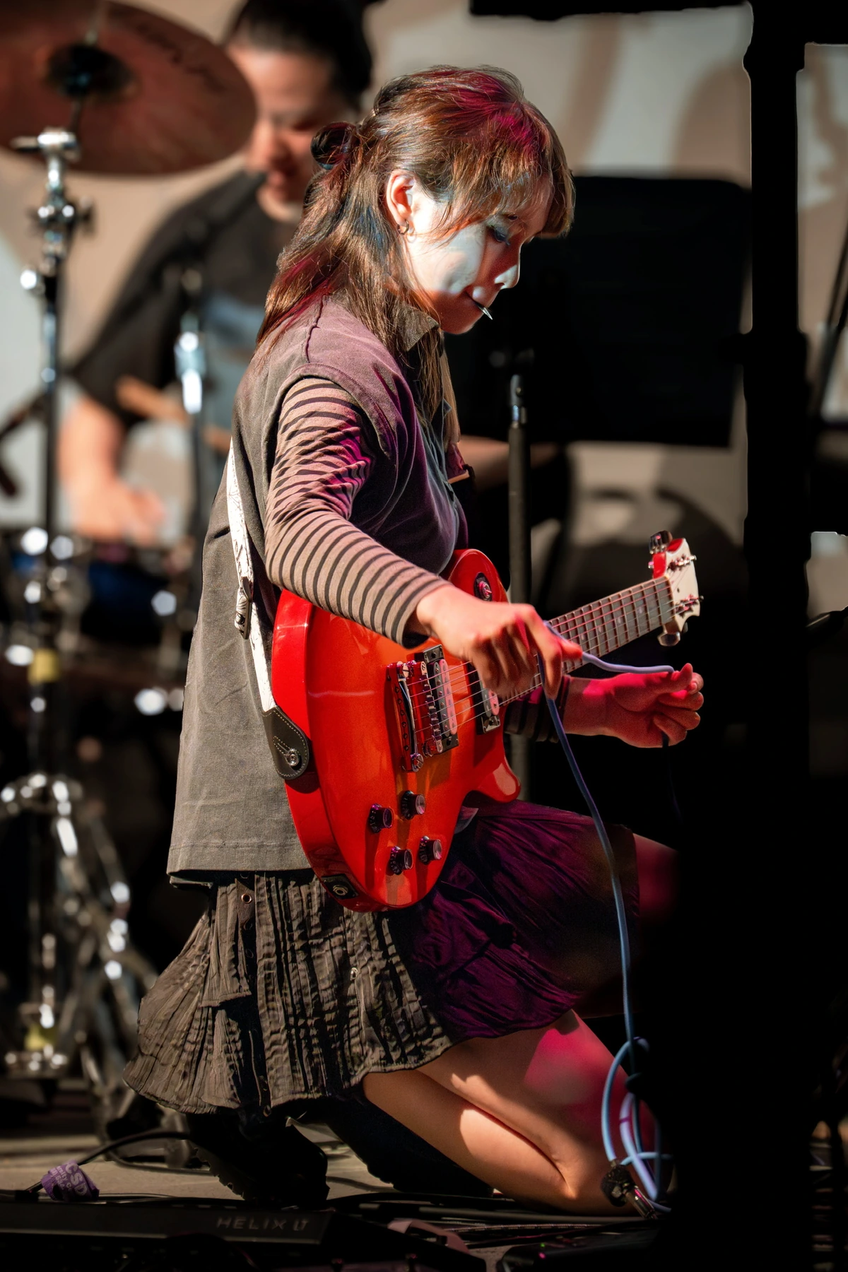 Cynthia playing a red electric guitar on stage with her band